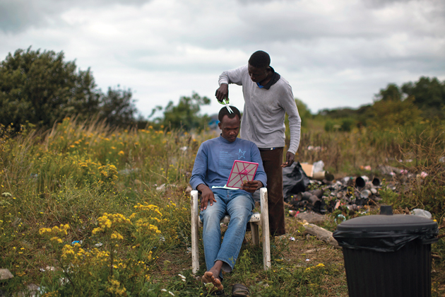 A Sudanese man gets a haircut at a camp near Calais early in August. / Photo: AP ,Calais, migrants, baptists, methodists, Church of Scotland, Cameron, Migration