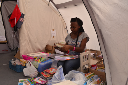 The tent with the school supplies with a volunteer classifying the donations. / J. Philippe