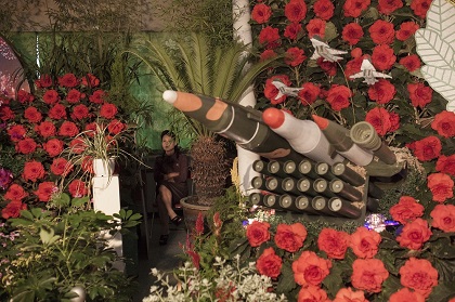 A woman sits next to models of military weapons at a festival for the Kimilsungia and Kimjongilia flowers, named after the country's late leaders, in Pyongyang, North Korea, 24 July 2013. / David Guttenfelder