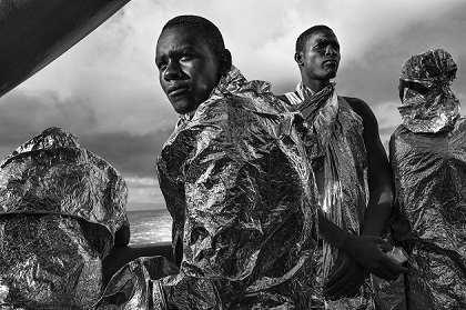Migrants wrapped in emergency blankets two days after being rescued catch sight of the Italian coast for the first time; Strait of Sicily, Mediterranean Sea, 23 August 2015. / Francesco Zizola, Italy.