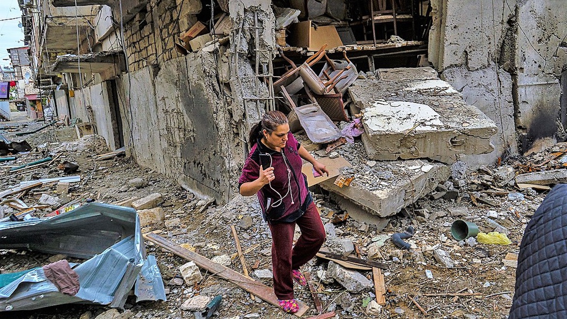 A woman walks among ruins in a village in the Republic of Artsakh bombed by Azerbaijan, October 2020. / Yan Boechat, VOA, Wikimedia Commons.,