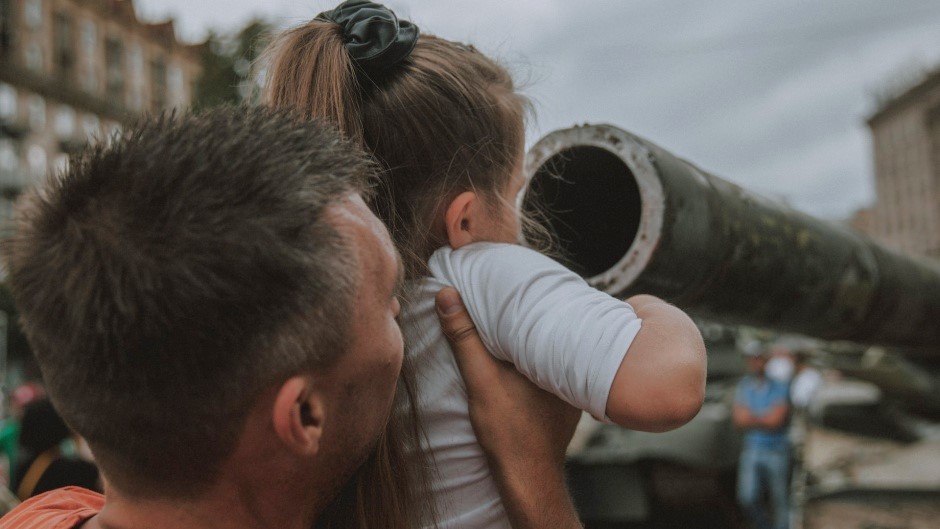 A father and child look at the wreckage of a Russian tank in Kyiv. / Photo: <a target="_blank" href="https://unsplash.com/@nick_tsybenko">Nick Tsybenko</a>, Unsplash, CC0.,