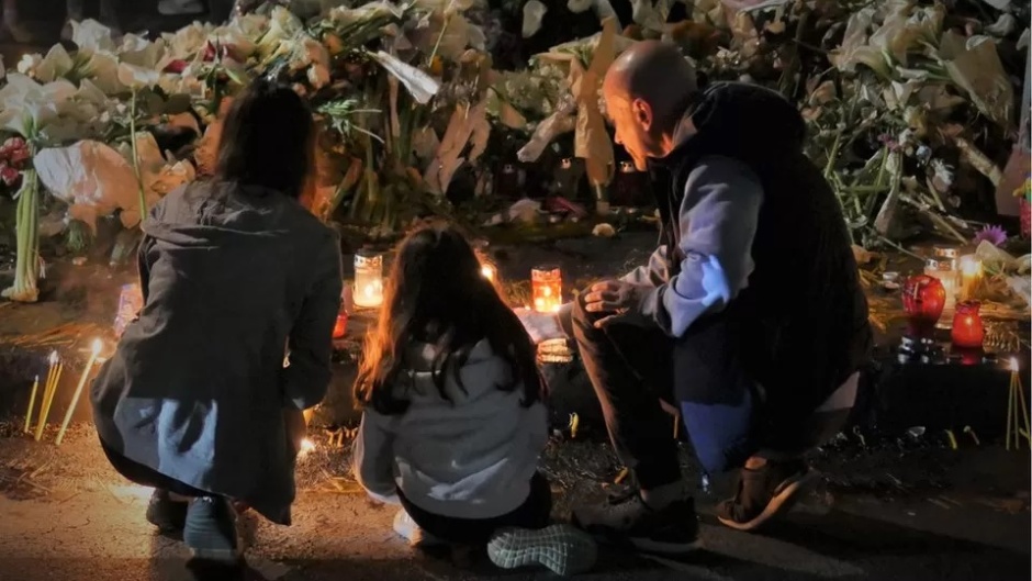 A family lights candles in memory of children killed in Belgrade mass shooting. / Photo: [link]BBC[link].,
