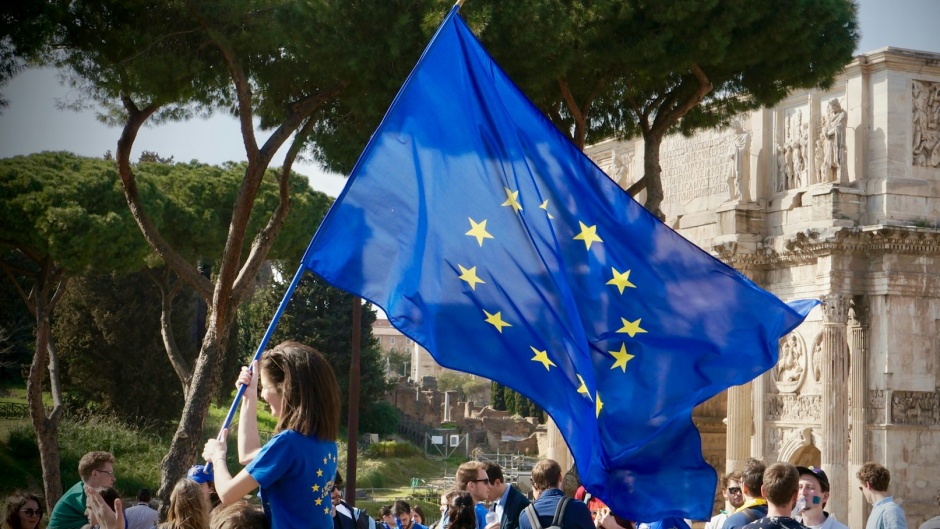 A woman with an European Union flag in Italy. / Photo: <a target="_blank" href="https://unsplash.com/@antoine_schibler">Antoine Schibler</a>,