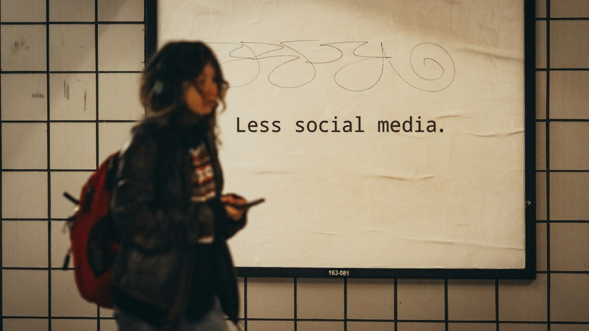 Woman passes by sign about reducing the use of social media. / Photo: <a target="_blank" href="https://unsplash.com/@jontyson">John Tyson</a>.,