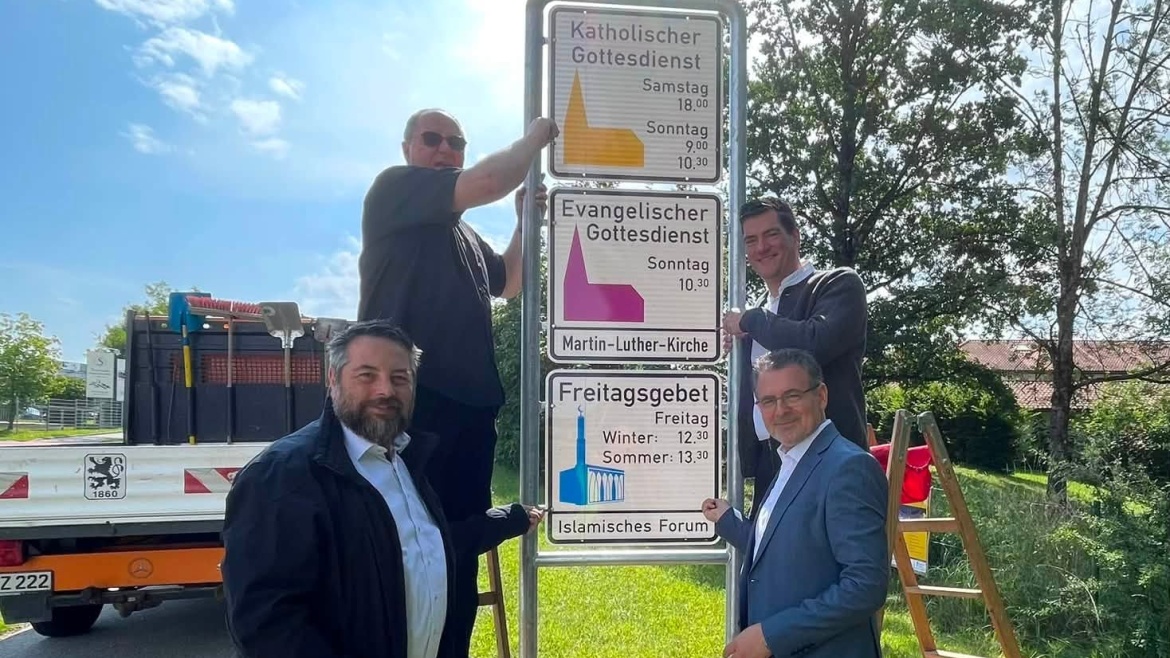 From left to right, the Mayor of Penzburg, the priest of the Catholic parish, the reverend of the Protestant parish, and the imam of the mosque; with the new sign including Muslim prayers. / Photo: <a target="_blank" href="https://islam-penzberg.de/">Penzburg mosque</a>.,